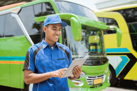 male-bus-crew-member-uniform-hat-smiles-while-using-digital-tablet-against-backdrop-bus-fleet
